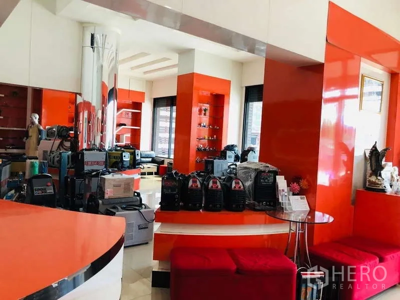 Shophouse for rent or sale in Bang Khun Thian, Bangkok - Spacious showroom with equipment displays, orange columns, bench seating and natural light.