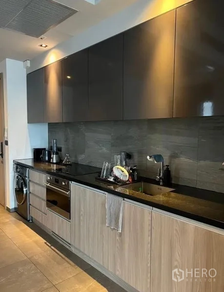 Condominium for rent in Watthana, Bangkok - Close-up of modern kitchen with stone backsplash, black countertop and ample storage.