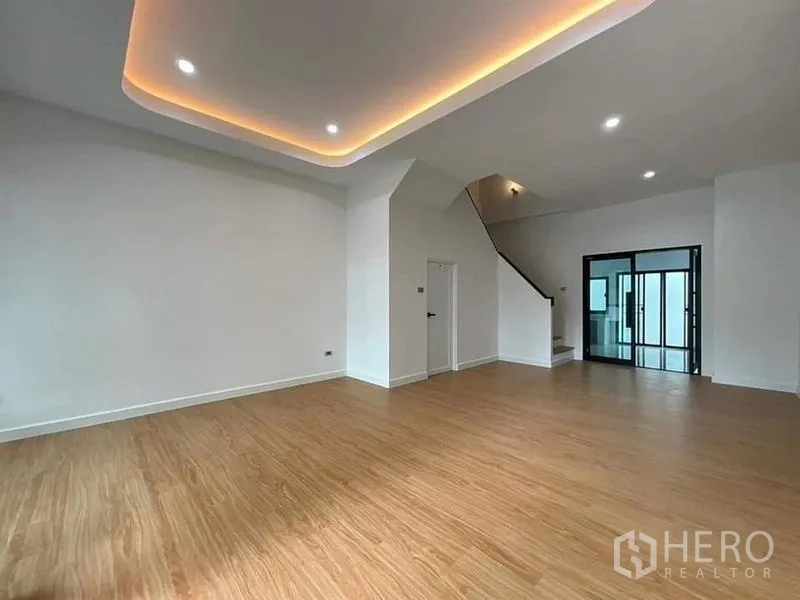 Townhouse for sale in Watthana, Bangkok - Large living room with cove lighting ceiling, staircase and sliding glass doors.