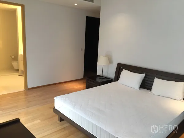 Condominium for rent or sale in Watthana, Bangkok - Spacious bedroom with king bed, wood flooring and an entrance to an ensuite bathroom.