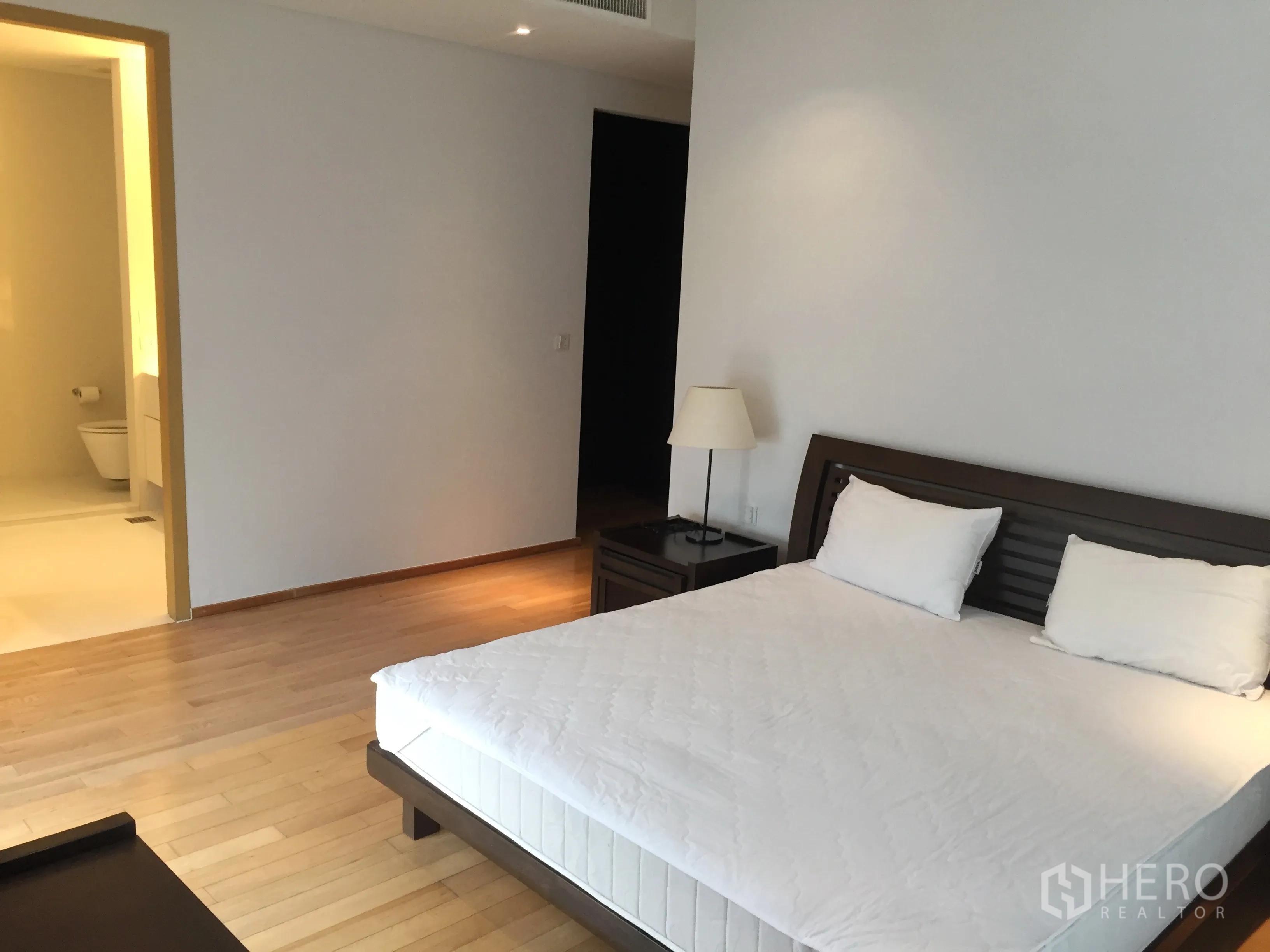 Condominium for rent or sale in Watthana, Bangkok - Spacious bedroom with king bed, wood flooring and an entrance to an ensuite bathroom.