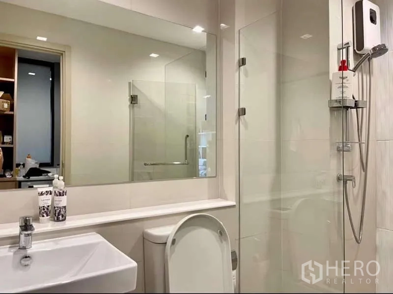 Condominium for rent in Pathum Wan, Bangkok - Clean bathroom with large mirror, glass-enclosed shower and white fixtures