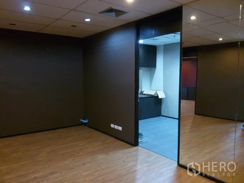 สำนักงาน ให้เช่าในWatthana, Bangkok - โซนสำนักงานผนังเข้ม ไฟดาวน์ไลท์ และประตูเชื่อมเข้าสู่แพนทรีพื้นกระเบื้องสีเทาพร้อมตู้เก็บของ