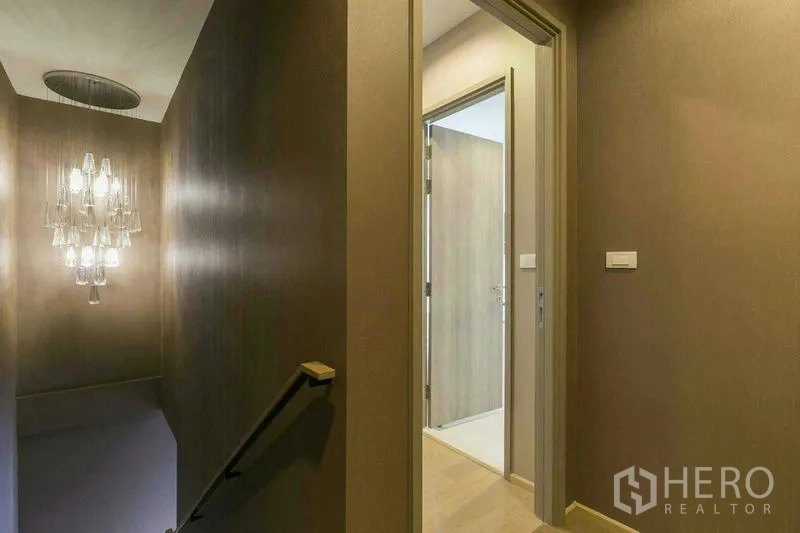 Condominium for rent or sale in Watthana, Bangkok - Hallway and stair landing with contemporary pendant chandelier and doorway to bathroom.