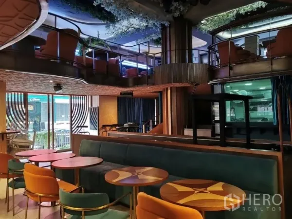 พื้นที่ขายปลีก ให้เช่า - เลานจ์เพดานสูงพร้อมโซฟาสีเขียว โต๊ะไม้ทรงกลม และที่นั่งชั้นลอย