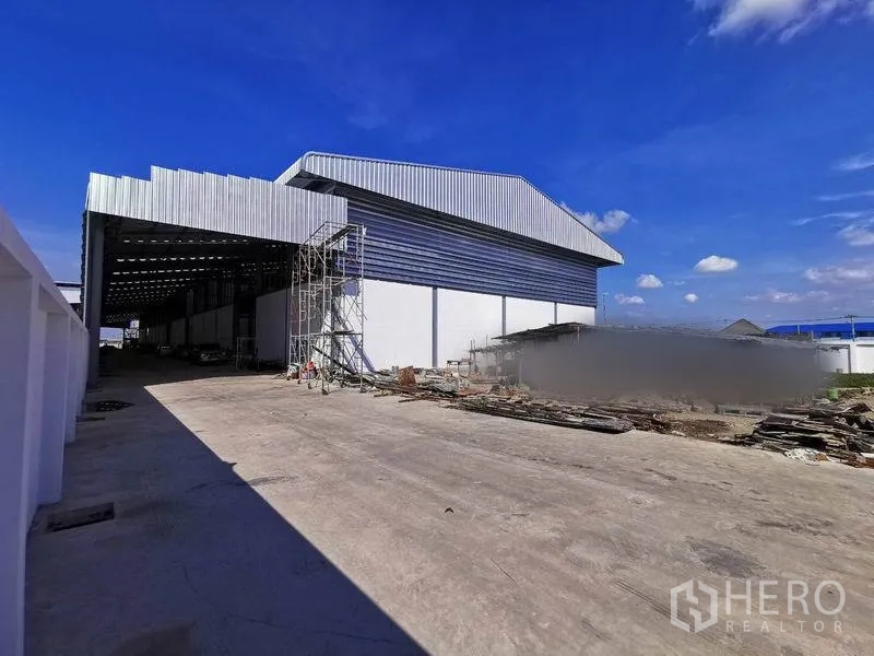 คลังสินค้า ให้เช่าในBang Phli, Samut Prakan - ด้านข้างอาคารมีชายคา นั่งร้าน และลานคอนกรีตกว้างใต้ท้องฟ้าสดใส