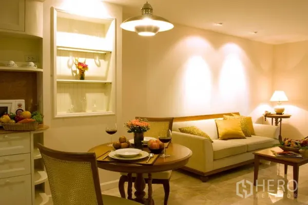 Apartment for rent in Bang Rak, Bangkok - Cozy breakfast nook beside a sofa with warm wall lighting and built-in display shelves near the kitchen.