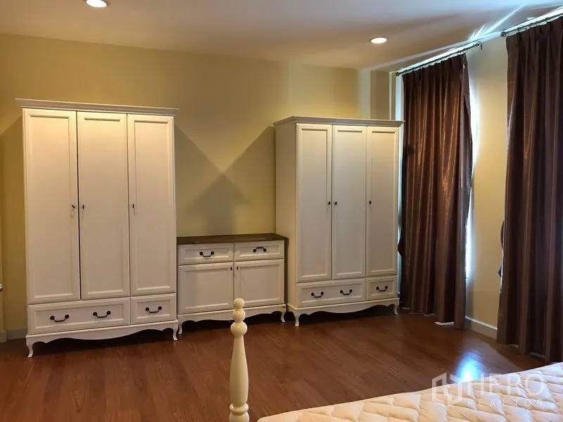 Townhouse for rent in Wang Thonglang, Bangkok - Bedroom with matching white wardrobes and dresser, brown curtains and wood floors.