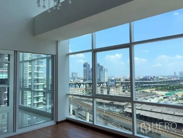 公寓 出售在Bang Na, Bangkok - 明亮转角客厅，落地窗俯瞰邦那城市景观与高架轨道。