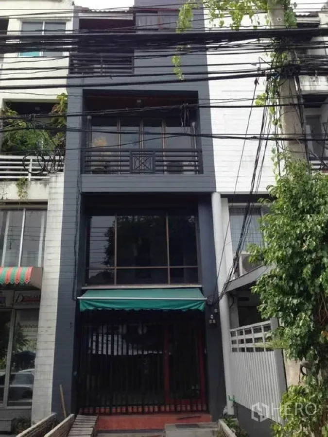 Home Office for rent or sale in Wang Thonglang, Bangkok - Full exterior of a townhouse-style home office with dark cladding, balconies and visible overhead power lines.