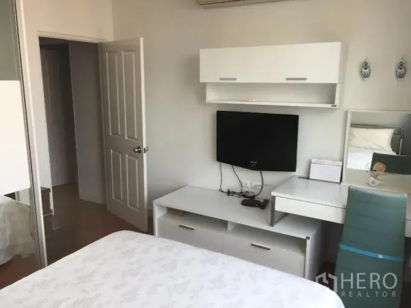 公寓 出租或出售在Khlong Toei, Bangkok - 明亮卧室，白色家具、壁挂电视、书桌与推拉衣柜。