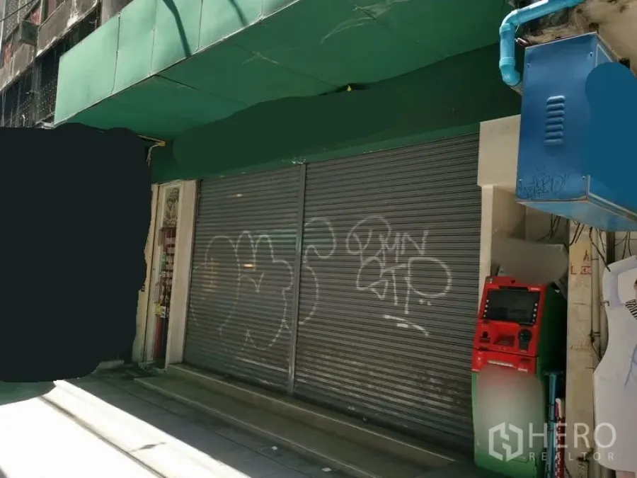 店屋 出租在Bangkok - 临街店铺外立面，绿色雨棚与关闭的金属卷闸门。