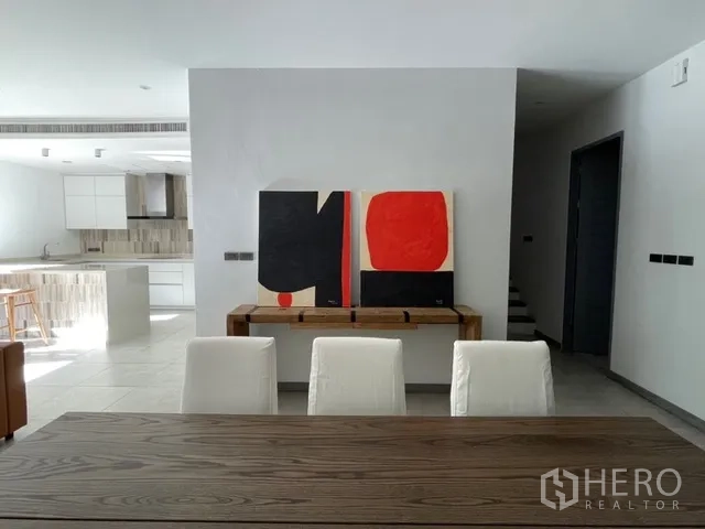 Detached House for rent in Watthana, Bangkok - Dining area with wooden table facing a modern kitchen and wall art.