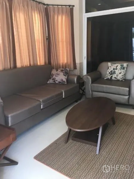 Detached House for rent in Bang Kapi, Bangkok - Living room with gray sofa set, armchair and coffee table beside full-height windows.