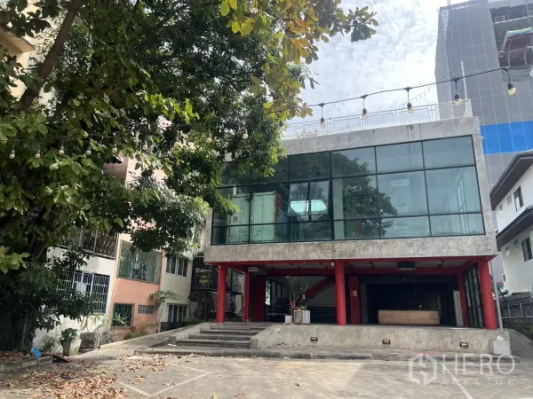 独立商业地产 出租在Din Daeng, Bangkok - 现代玻璃外墙近景，红色立柱与入口台阶。