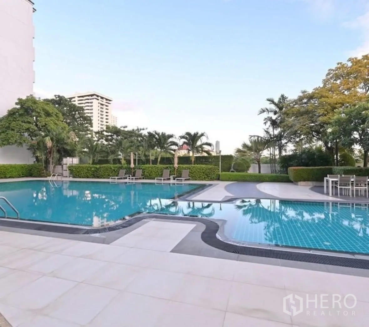 Condominium for rent or sale in Watthana, Bangkok - Outdoor swimming pool with sun loungers, palm trees, and seating areas.