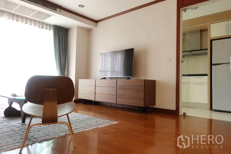 Condominium for rent in Khlong Toei, Bangkok - Bright living room with wood floors, TV on low console and glass door to the kitchen.