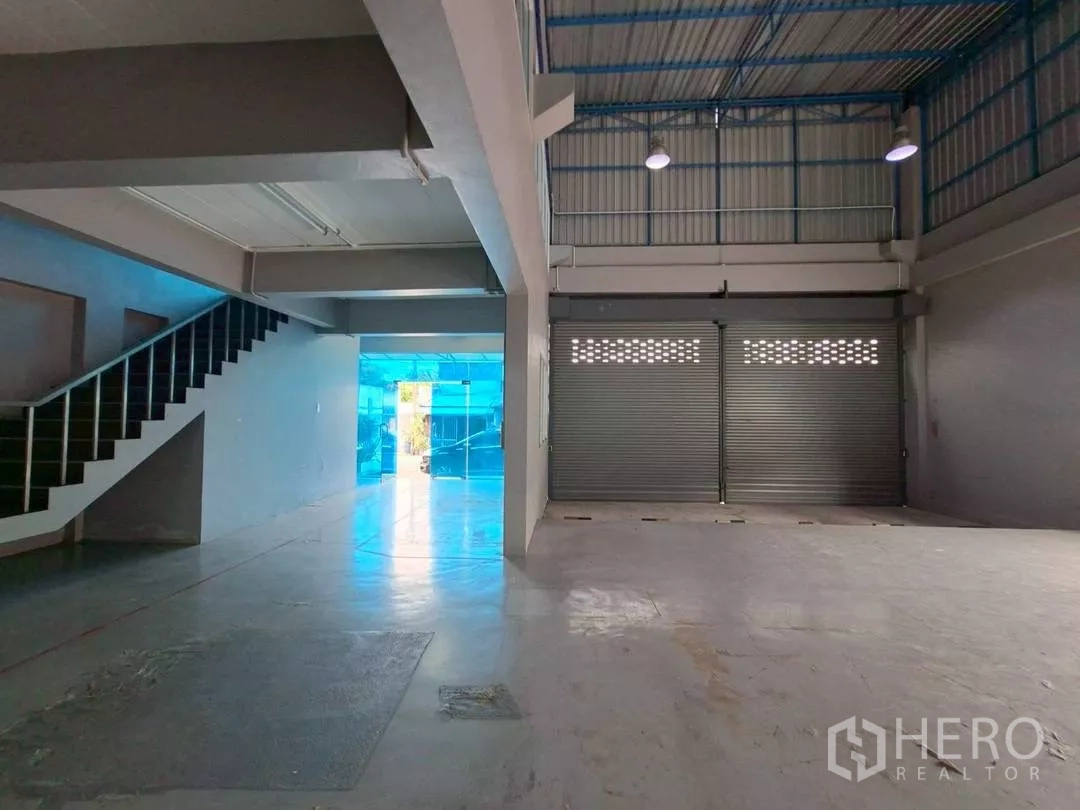 Warehouse for rent in Suan Luang, Bangkok - Warehouse floor showing staircase and two roller shutters by the entrance.