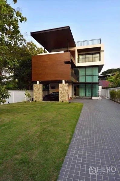 Townhouse for rent in Din Daeng, Bangkok - Modern three-storey townhouse exterior with wood cladding, stone pillars, long driveway and front lawn.