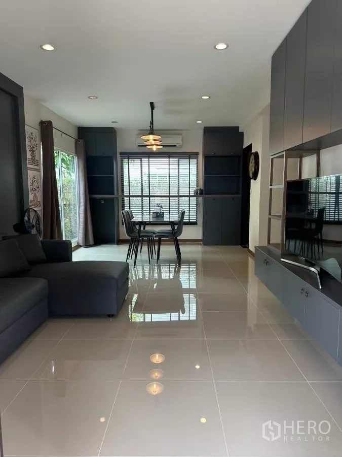 บ้าน ให้เช่าในSuan Luang, Bangkok - ห้องนั่งเล่นสว่าง พื้นกระเบื้องเงา โซฟาสีเทา ชุดโต๊ะอาหาร และตู้บิวท์อินริมหน้าต่างบานใหญ่.