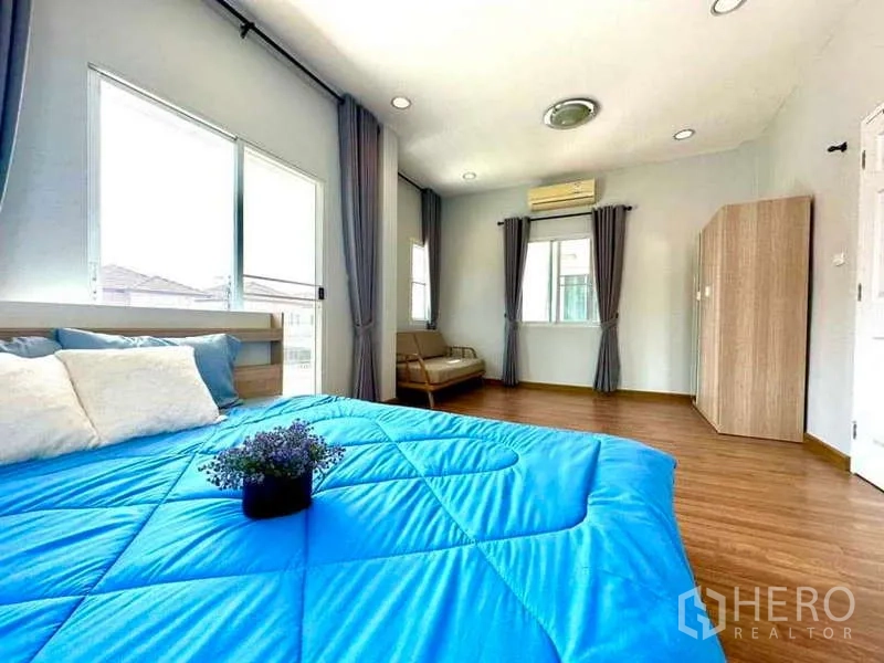 บ้าน ให้เช่าในLat Krabang, Bangkok - ห้องนอนใหญ่กว้าง เตียงผ้าห่มสีน้ำเงิน หน้าต่างหลายบาน และเครื่องปรับอากาศ