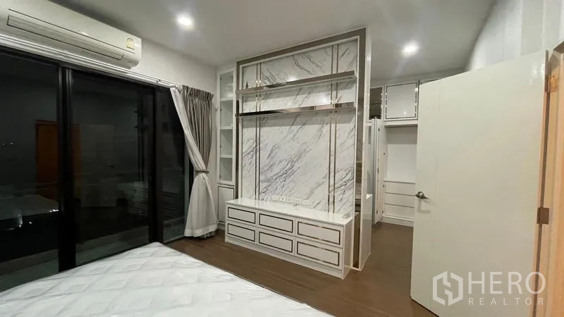 Detached House for rent or sale in Prawet, Bangkok - Bedroom with marble-look media wall, balcony sliding doors and wood flooring.