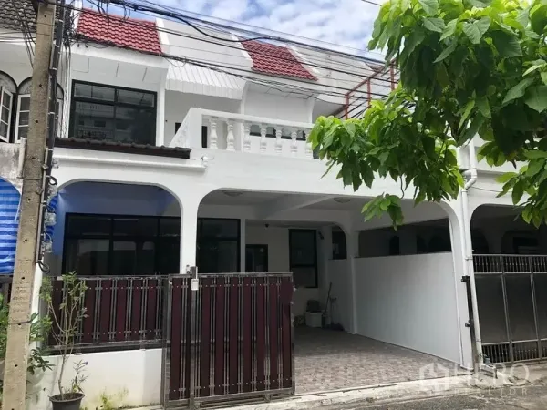 Townhouse for rent in Watthana, Bangkok - Two-storey white townhouse exterior with red roof tiles, gated entrance and covered carport on a quiet lane.