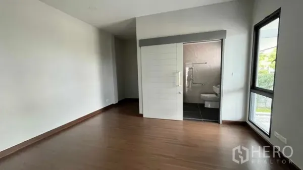 Detached House for sale in Bang Phli, Samut Prakan - Bedroom with corner window and ensuite bathroom accessed by a sliding door.