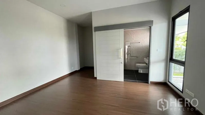 Detached House for sale in Bang Phli, Samut Prakan - Bedroom with corner window and ensuite bathroom accessed by a sliding door.