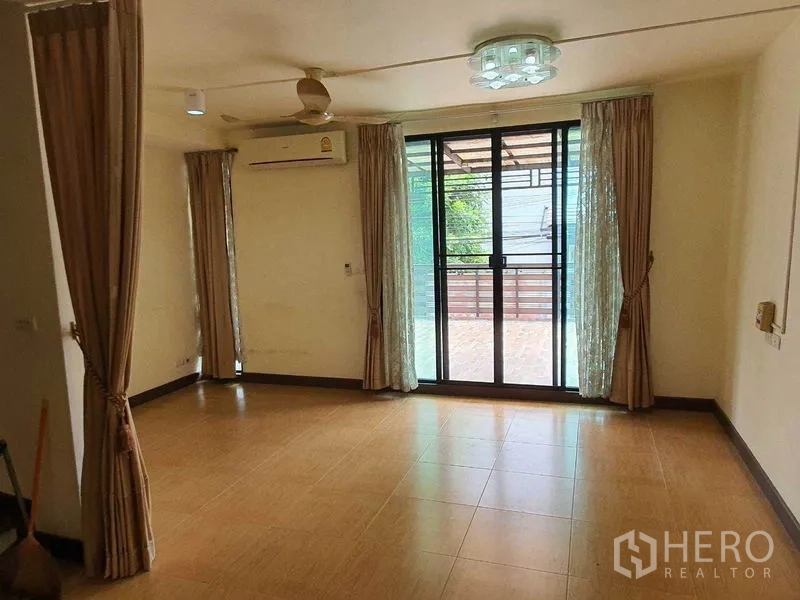 Townhouse for sale in Khlong Toei, Bangkok - Living room opening to a balcony via large sliding glass doors and curtains.