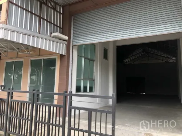 联排别墅 出售在Bang Bua Thong, Nonthaburi - 前方装卸区，超高卷帘门，旁设玻璃办公室与金属雨棚。