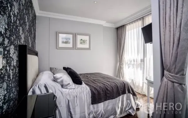 Condominium for rent or sale in Khlong Toei, Bangkok - Second bedroom with patterned accent wall, double bed and sheer curtains.