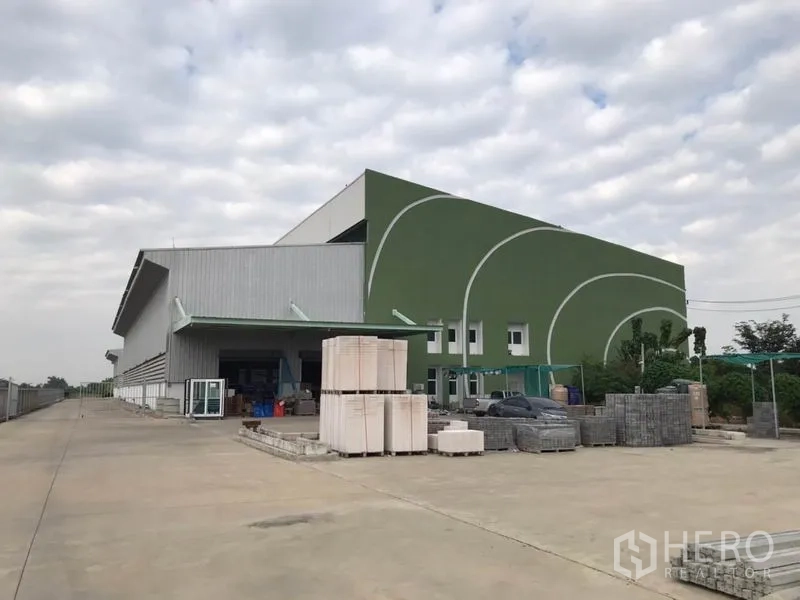 Warehouse for rent in Sai Noi, Nonthaburi - Modern warehouse exterior in Sai Noi with green facade, covered loading bay and wide concrete yard.