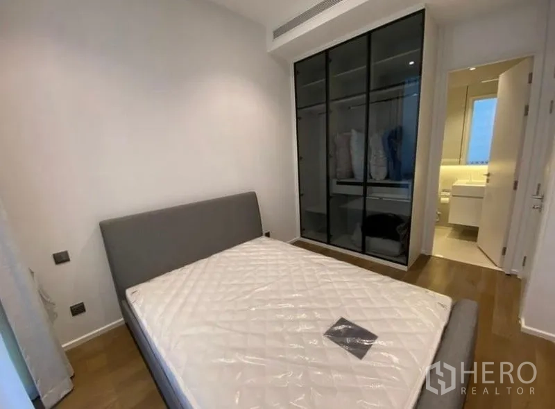 Condominium for rent in Pathum Wan, Bangkok - Second bedroom with bed, floor-to-ceiling wardrobe with glass doors, and access to a bright bathroom.