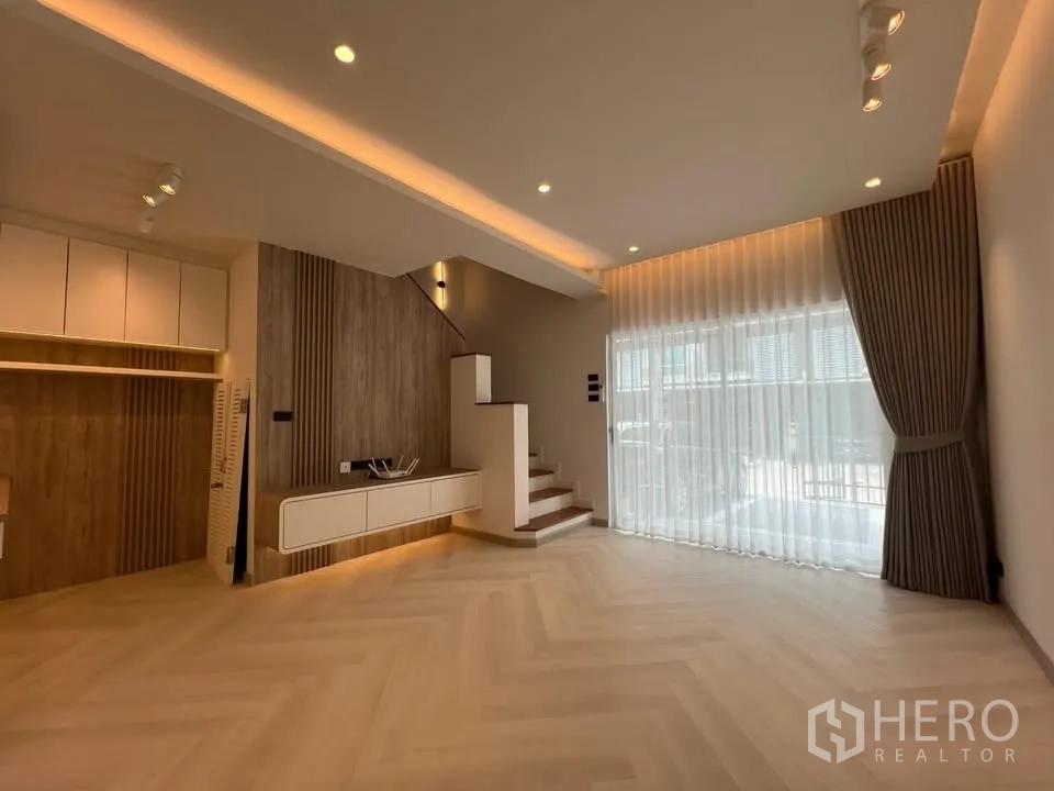 Townhouse for rent in Prawet, Bangkok - Living room with staircase, feature wall and wide window with sheer curtain.