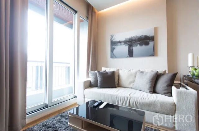 Condominium for rent in Ratchathewi, Bangkok - Bright living room with sofa, sliding glass doors to a balcony and city view in a Ratchathewi condo.