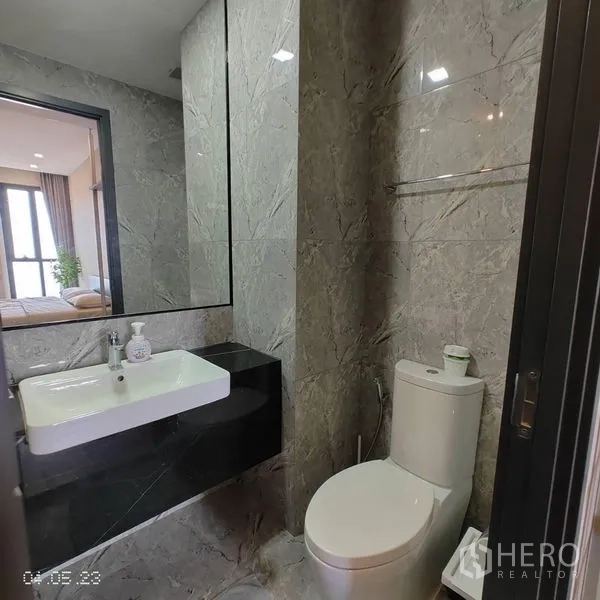 Condominium for rent in Watthana, Bangkok - Modern bathroom with marble-style tiles, large mirror, vanity and toilet.