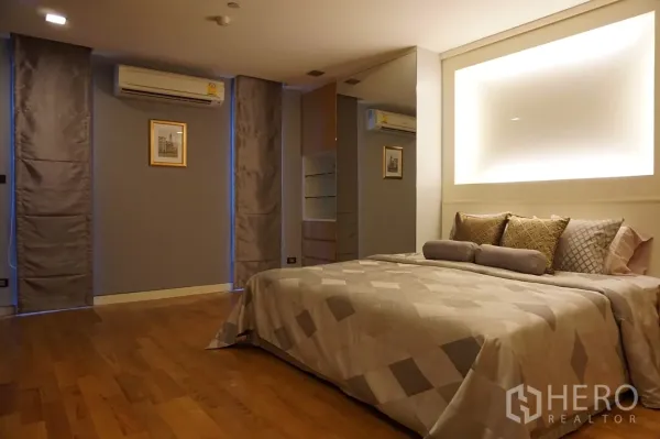 Condominium for rent or sale in Bang Rak, Bangkok - Spacious bedroom with king bed, accent lighting, mirrored wardrobe, air conditioning and wood floors in a Bang Rak condominium.