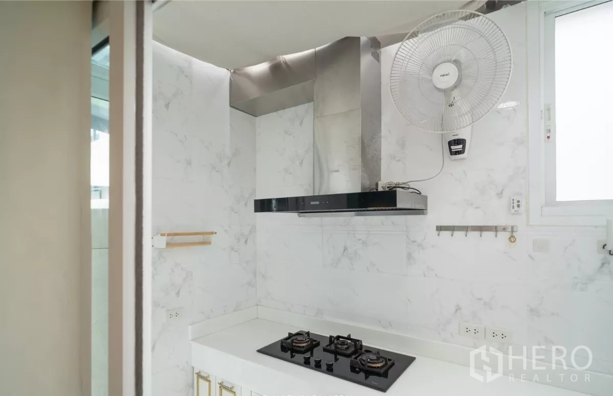 Detached House for rent or sale in Saphan Sung, Bangkok - Thai kitchen with gas cooktop, chimney hood, marble‑look walls and wall fan.
