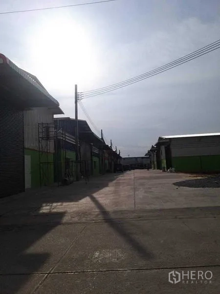 Warehouse for rent in Bang Khun Thian, Bangkok - Wide driveway running through the warehouse complex in daylight.