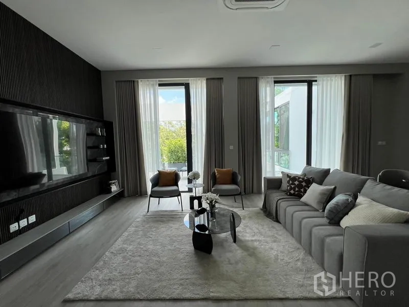 Detached House for rent in Saphan Sung, Bangkok - Family lounge opening to balconies with floor-to-ceiling windows and a dark feature wall.