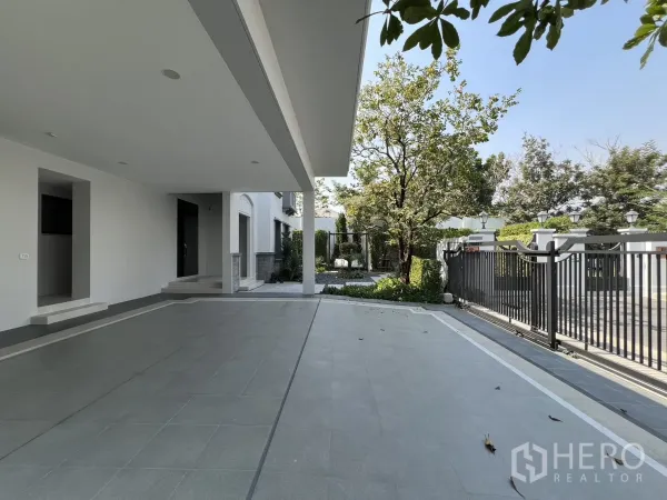 Detached House for rent in Saphan Sung, Bangkok - Spacious carport and entrance looking toward black gate and greenery.