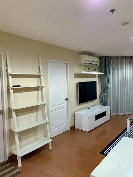 Condominium for rent in Huai Khwang, Bangkok - Bright living room with wall-mounted TV, white console, ladder shelf, air conditioner and floor-to-ceiling curtains.