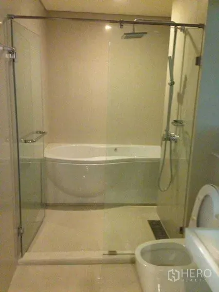 Condominium for rent or sale in Watthana, Bangkok - Modern bathroom featuring a glass-enclosed shower with rainfall head, separate soaking bathtub and toilet in neutral tones.