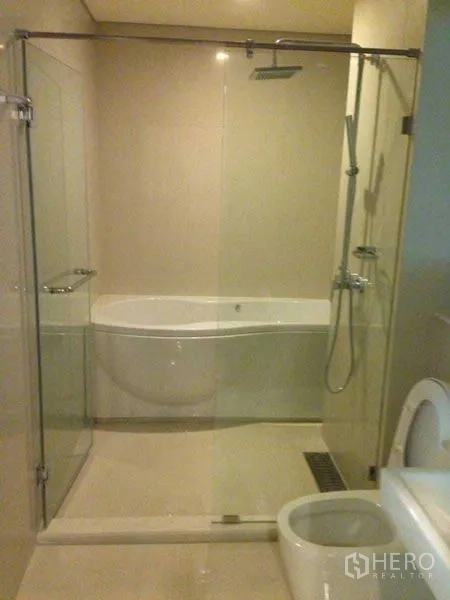 Condominium for rent or sale in Watthana, Bangkok - Modern bathroom featuring a glass-enclosed shower with rainfall head, separate soaking bathtub and toilet in neutral tones.