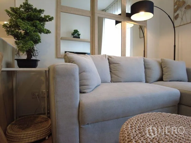 Condominium for sale in Watthana, Bangkok - Close-up of a cozy gray sectional sofa with floor lamp and indoor plant.