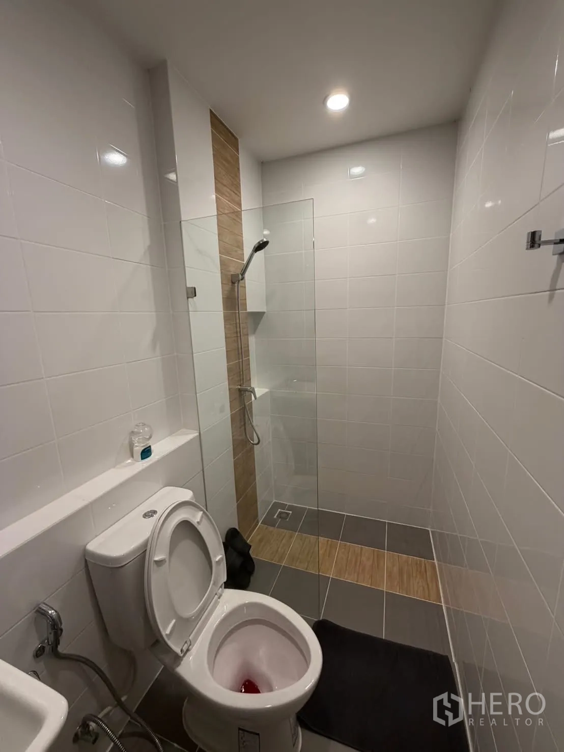 Townhouse for rent in Bang Phli, Samut Prakan - Bathroom featuring a walk-in shower with glass screen, grey tiles, wood-look accent and toilet.