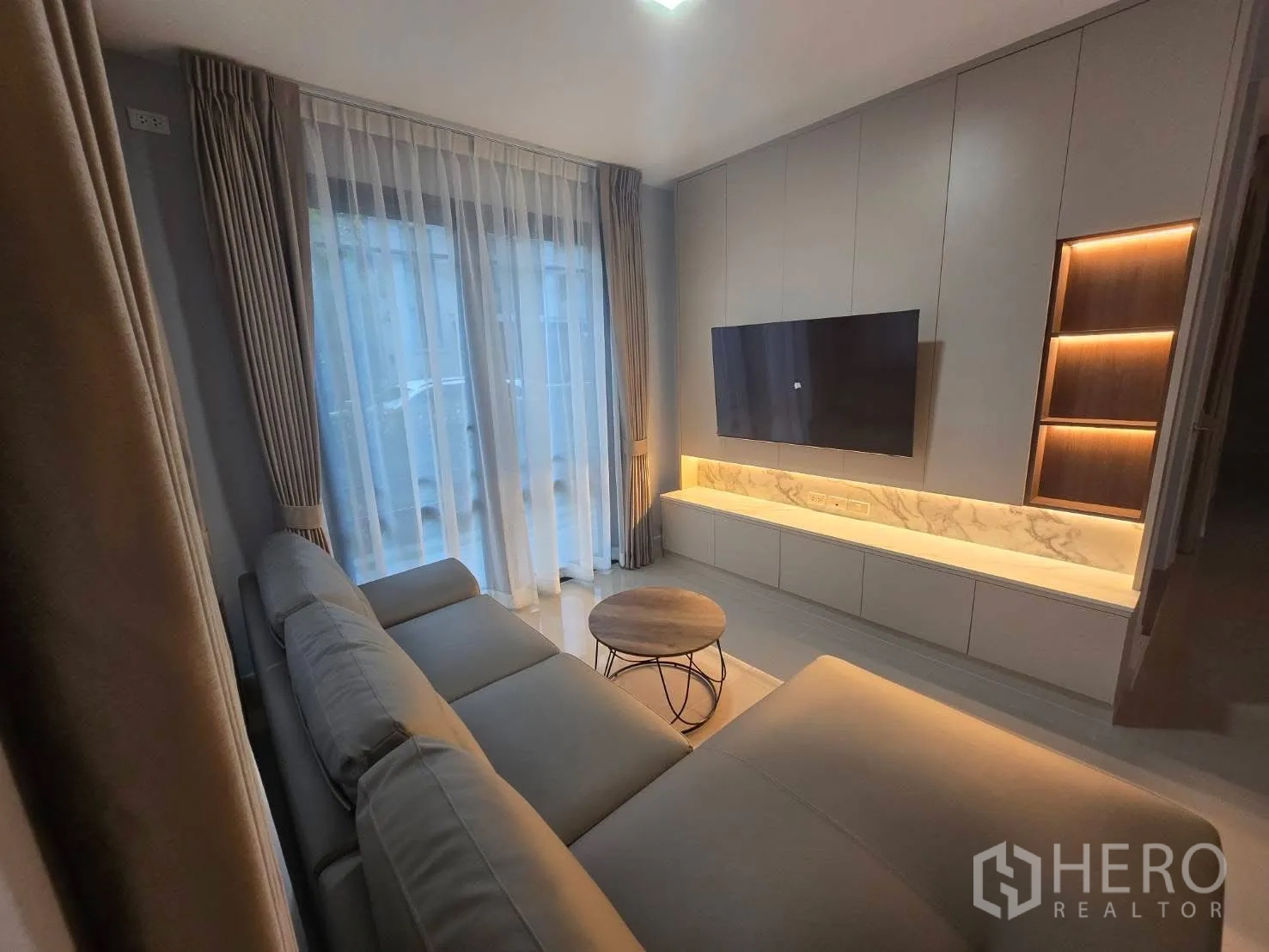 Semi-detached House for rent in Bang Phli, Samut Prakan - Living room with L-shaped sofa, mounted TV, and backlit cabinetry.