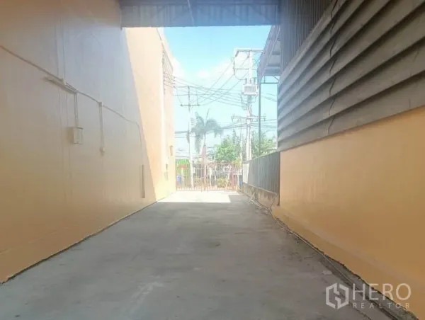 คลังสินค้า ให้เช่าในPathum Thani - ทางรถเข้าออกแบบลอดหลังคา มุ่งสู่ประตูรั้วหน้าและแนวสายไฟริมถนน.