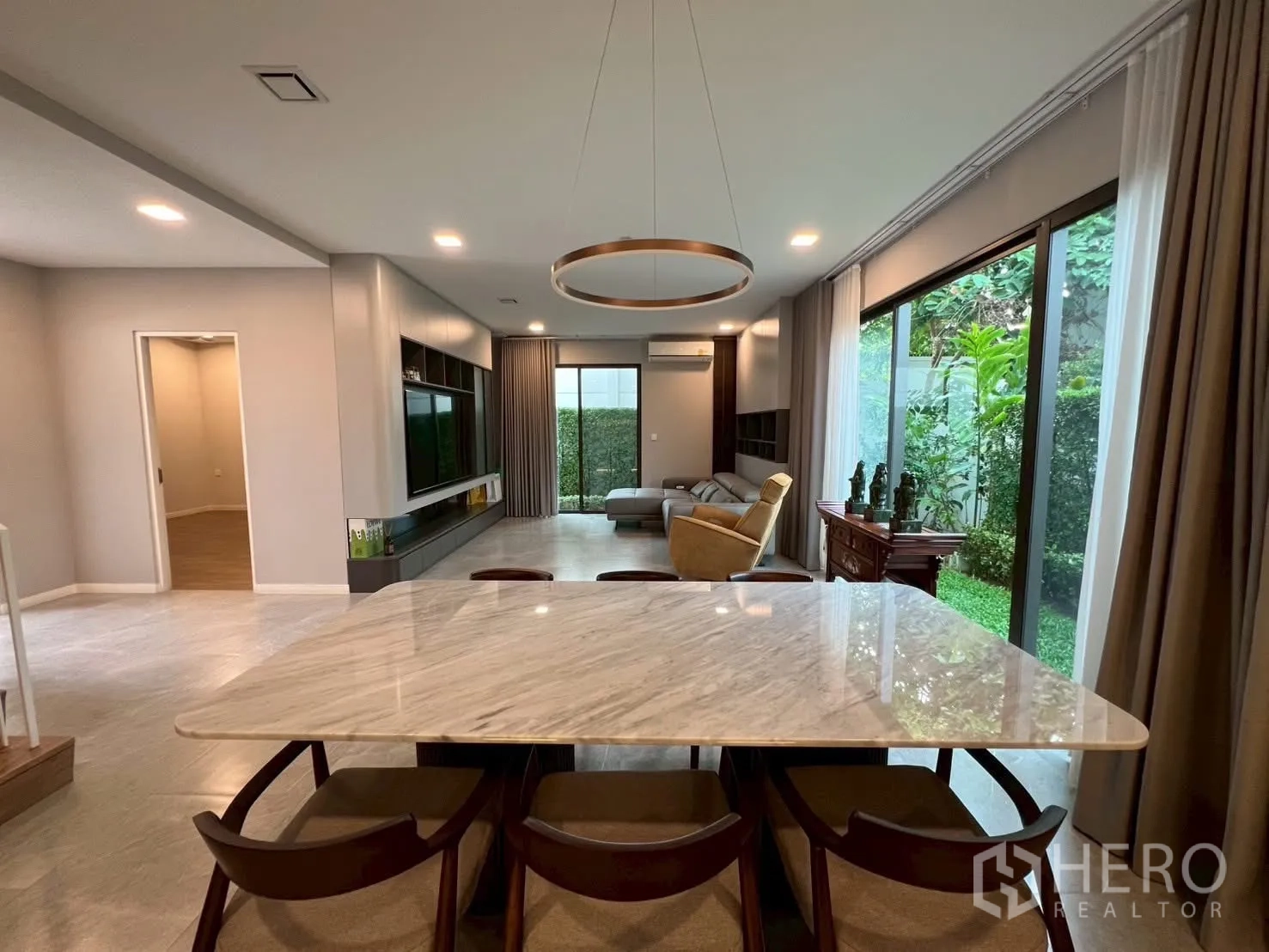 Detached House for rent in Samut Prakan - Dining zone with circular chandelier overlooking the hedge-lined garden and living room.